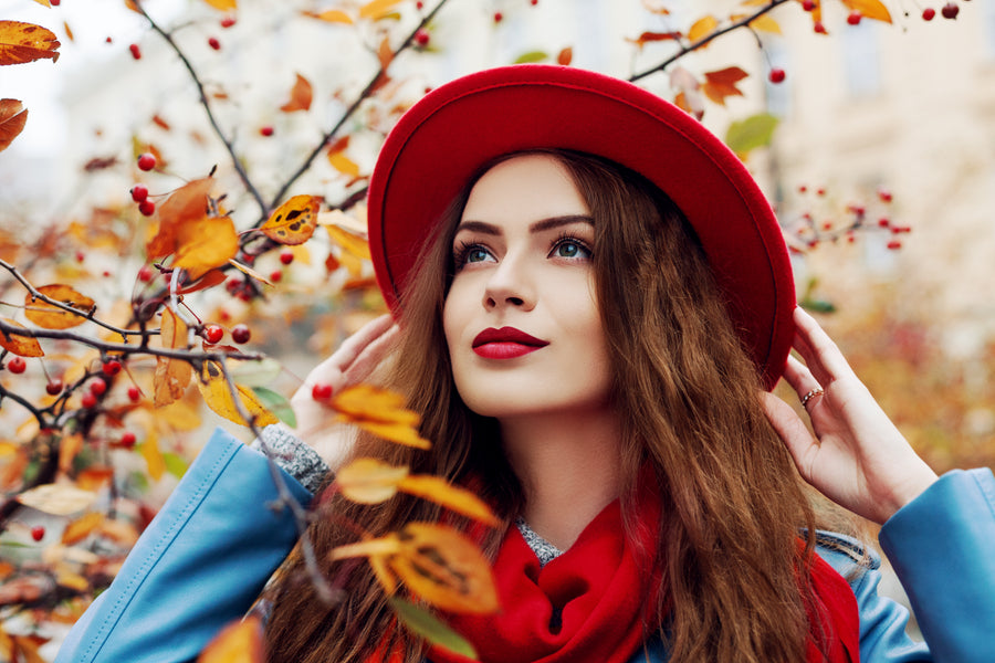 Woman wearing a red hat and scarf in an autumn setting with colorful leaves and berries.